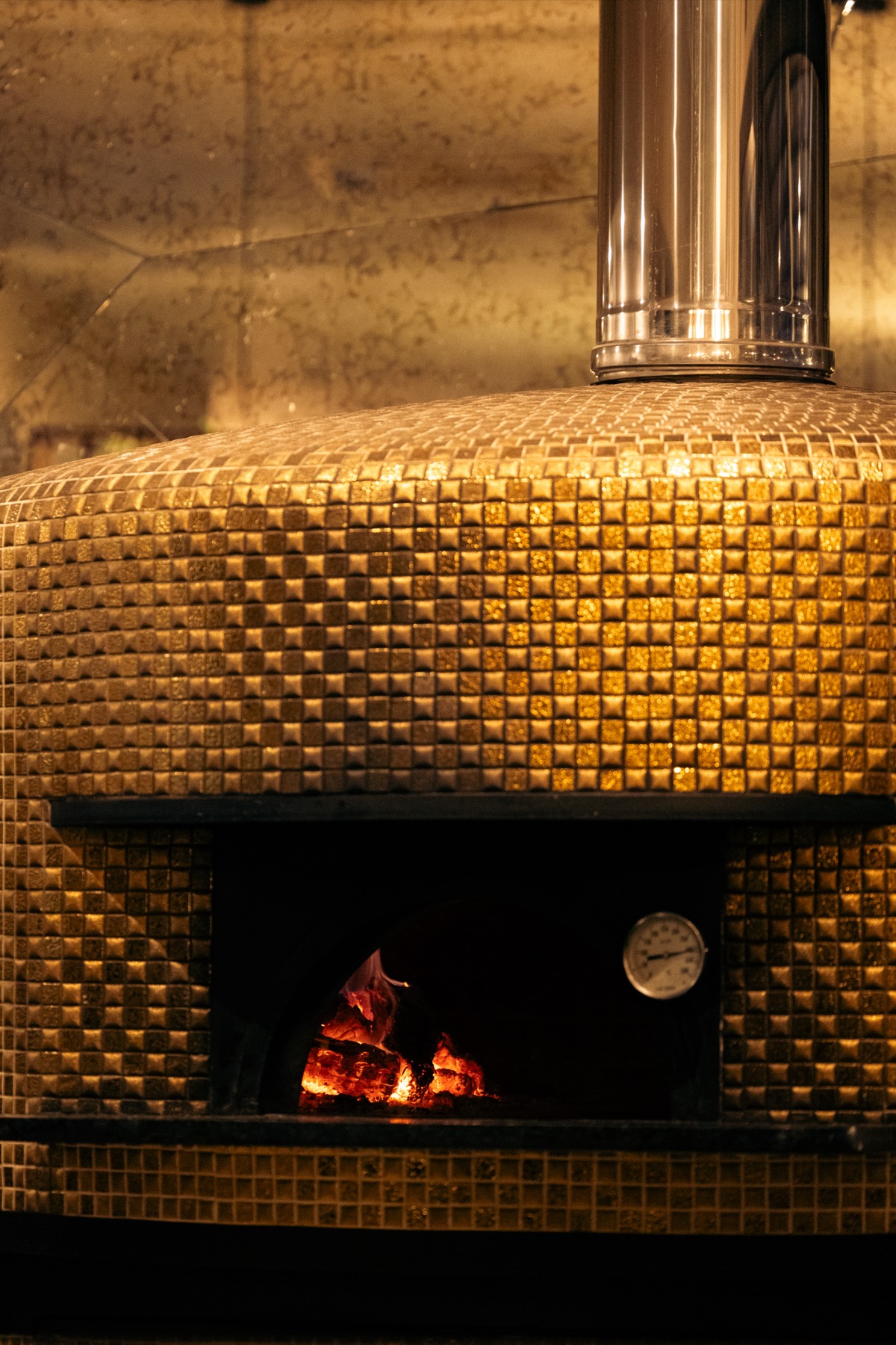Forno a lenha revestido a mosaico dourado com a chama acesa no interior